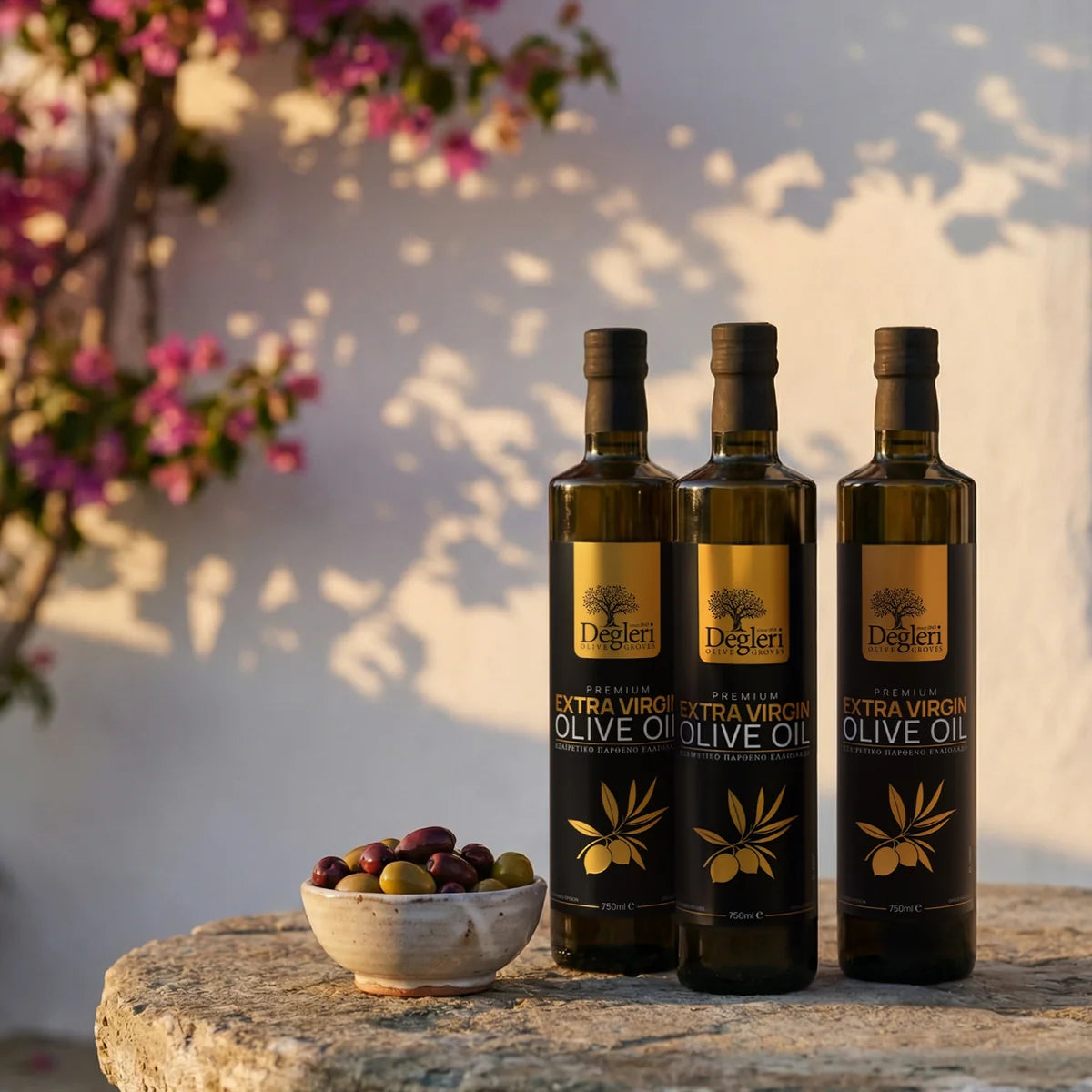 Three Degleri premium extra virgin olive oil bottles on a stone table with vibrant pink bougainvillea — Greek olive oil at golden hour