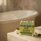 Degleri handmade jasmine olive oil soap bar on a marble bathroom surface next to a freestanding bathtub with fresh white jasmine flowers